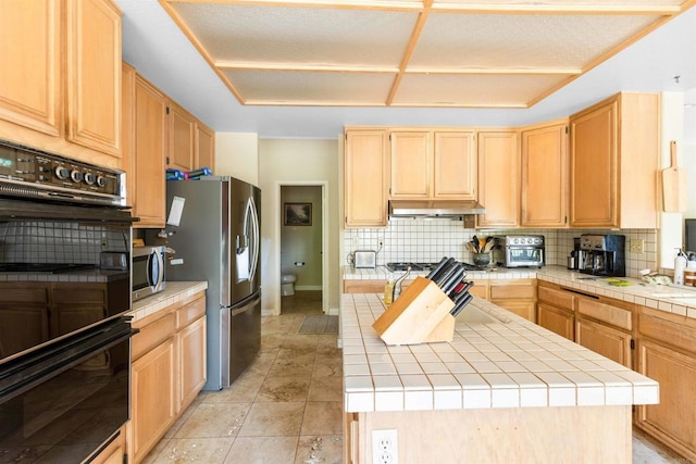 kitchen with light brown cabinets, stainless steel appliances, tile counters, a kitchen island, and backsplash