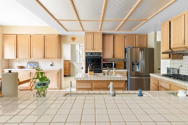 kitchen with appliances with stainless steel finishes, tile counters, light brown cabinets, and decorative backsplash
