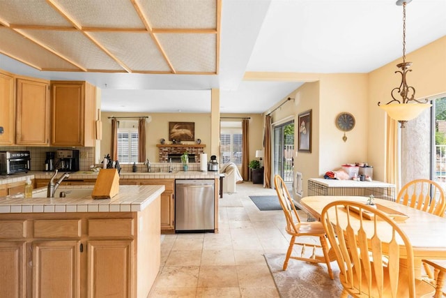 kitchen featuring a wealth of natural light, stainless steel dishwasher, tile counters, and a sink