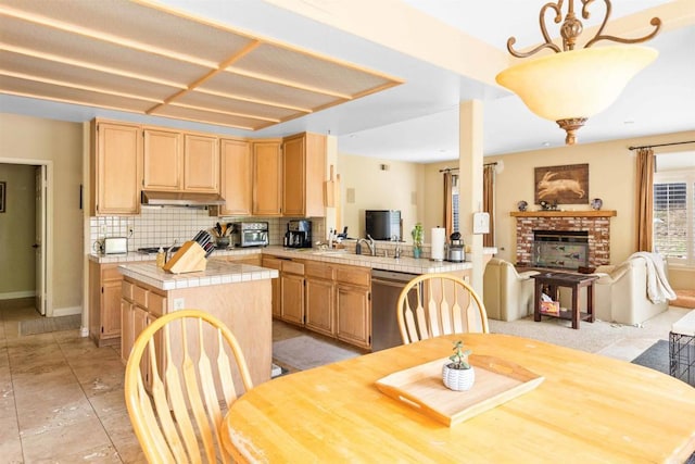 kitchen with stainless steel dishwasher, light brown cabinets, open floor plan, tile countertops, and backsplash