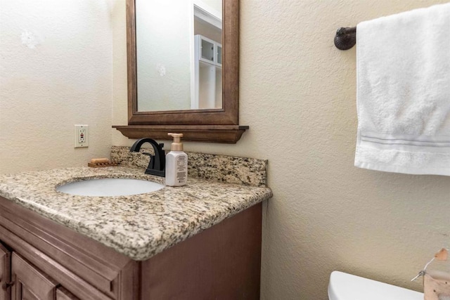 bathroom with toilet, a textured wall, and vanity
