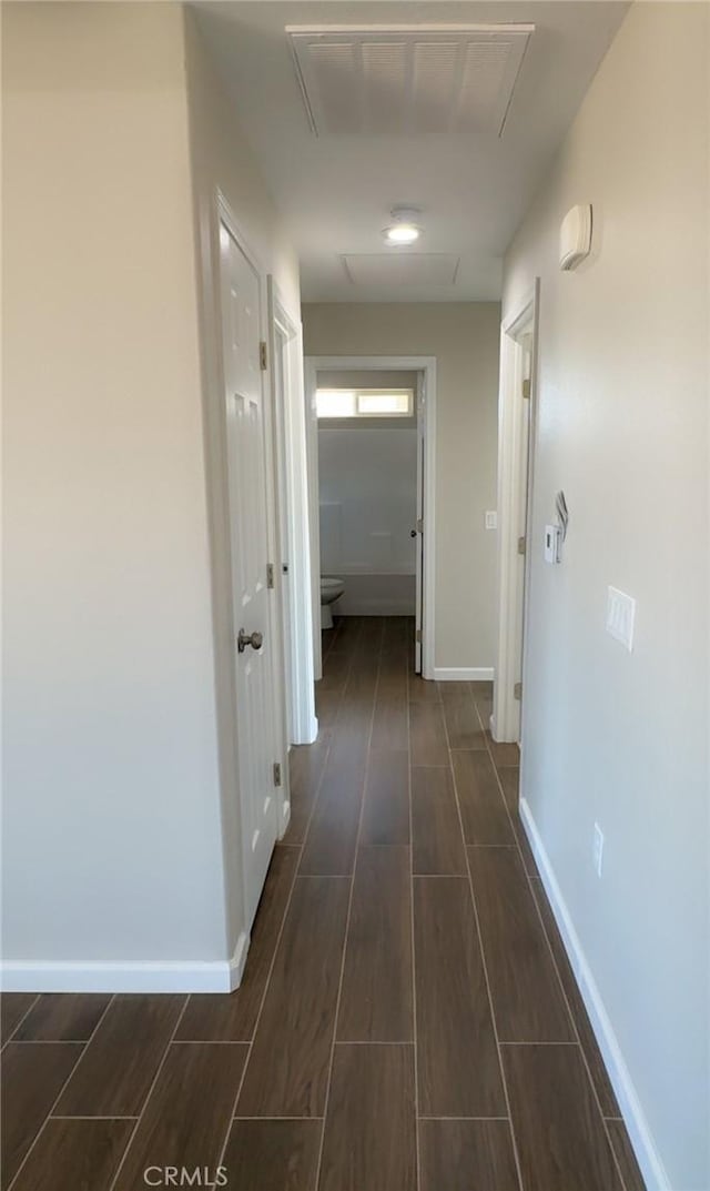 hall featuring wood tiled floor, visible vents, and baseboards