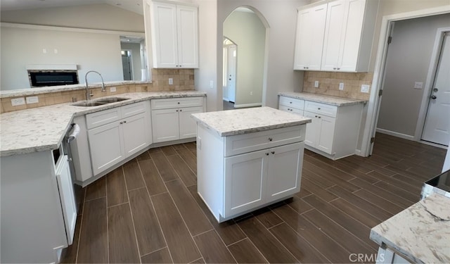 kitchen featuring light stone countertops, decorative backsplash, white cabinets, a sink, and wood finish floors