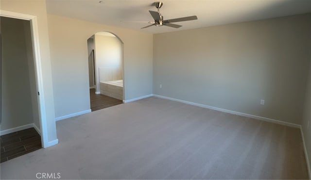 unfurnished room featuring baseboards, arched walkways, ceiling fan, and carpet