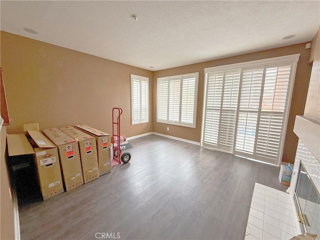 game room with a textured ceiling, baseboards, a brick fireplace, and wood finished floors