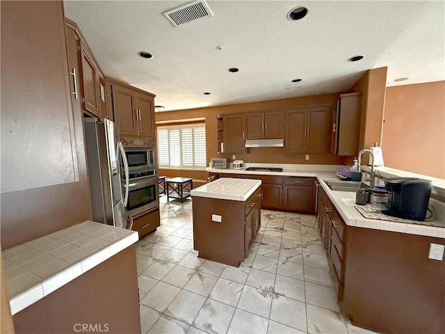 kitchen with visible vents, appliances with stainless steel finishes, a sink, tile counters, and under cabinet range hood