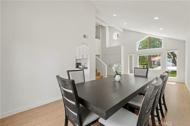 dining area featuring visible vents, baseboards, high vaulted ceiling, stairway, and light wood-style flooring