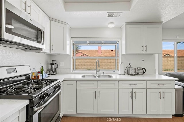kitchen with visible vents, light countertops, white cabinetry, a sink, and appliances with stainless steel finishes