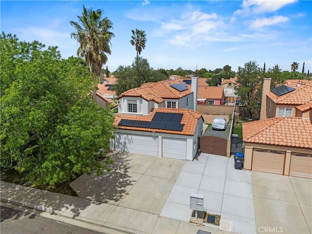 mediterranean / spanish-style home featuring a tiled roof, roof mounted solar panels, a residential view, and a gate