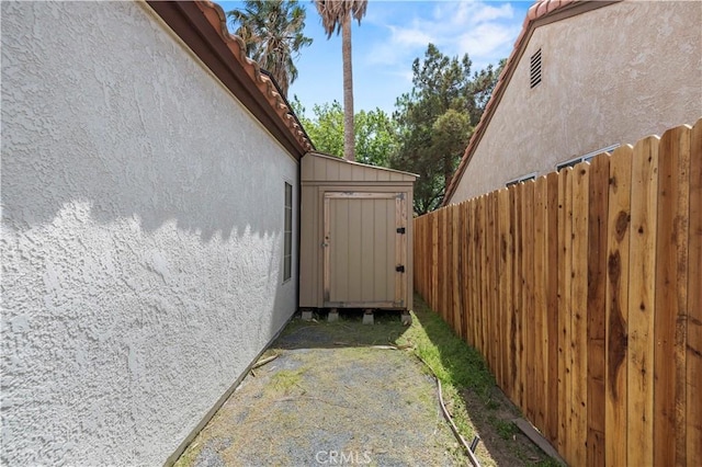 view of side of home featuring fence, a storage unit, an outbuilding, and stucco siding