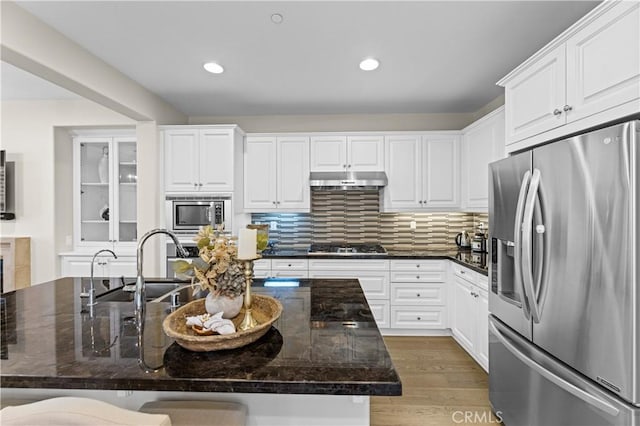 kitchen with backsplash, a sink, under cabinet range hood, stainless steel appliances, and white cabinetry