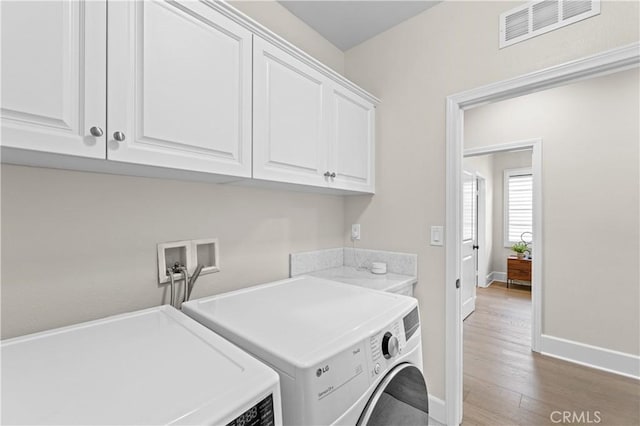 laundry area featuring visible vents, washing machine and dryer, wood finished floors, baseboards, and cabinet space