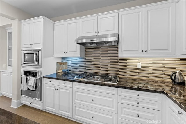 kitchen with under cabinet range hood, stainless steel appliances, white cabinetry, and tasteful backsplash