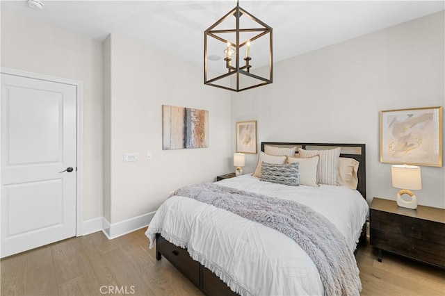 bedroom with baseboards, wood finished floors, and a notable chandelier