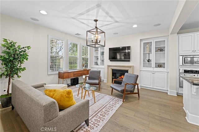 living area featuring recessed lighting, a chandelier, a glass covered fireplace, and light wood finished floors
