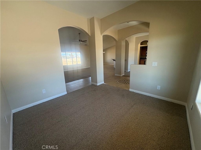 carpeted spare room with arched walkways, baseboards, and a ceiling fan