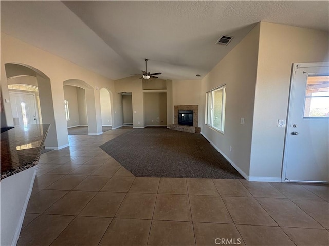 unfurnished living room featuring visible vents, a glass covered fireplace, lofted ceiling, dark tile patterned floors, and a ceiling fan