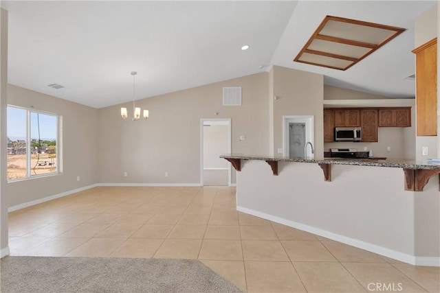 11569 Arroyo Ave, Hesperia, CA 92345 - kitchen featuring stainless steel microwave, a breakfast bar area, vaulted ceiling, stone counters, and light tile patterned flooring