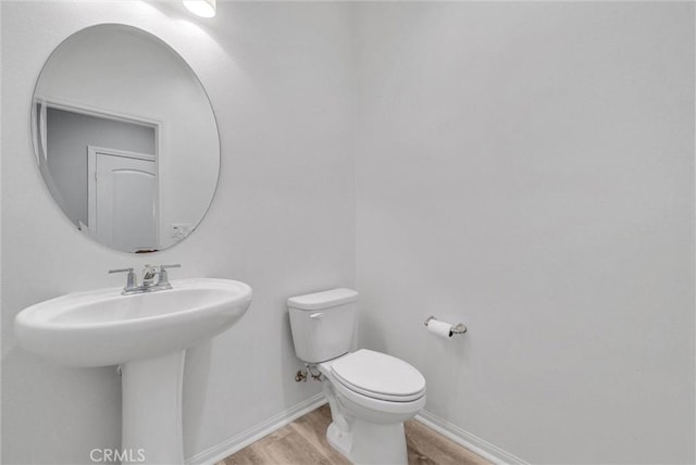 half bath with a sink, wood finished floors, toilet, and baseboards