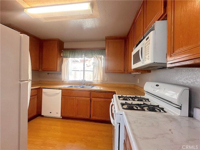kitchen featuring white appliances, brown cabinets, a sink, and light countertops