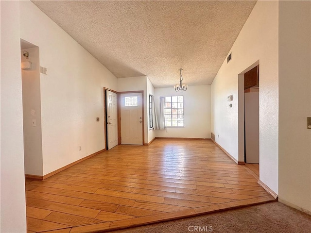 interior space with a textured ceiling, a notable chandelier, baseboards, and light wood-type flooring