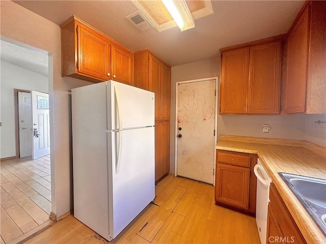 kitchen featuring visible vents, white appliances, light wood-style floors, light countertops, and a sink