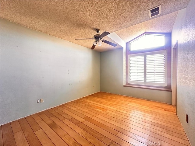 spare room with visible vents, lofted ceiling, a textured ceiling, hardwood / wood-style flooring, and a ceiling fan