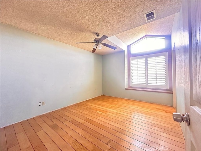empty room with visible vents, lofted ceiling, a textured ceiling, hardwood / wood-style flooring, and a ceiling fan
