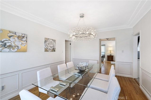 dining space with crown molding, a decorative wall, wood finished floors, and a notable chandelier