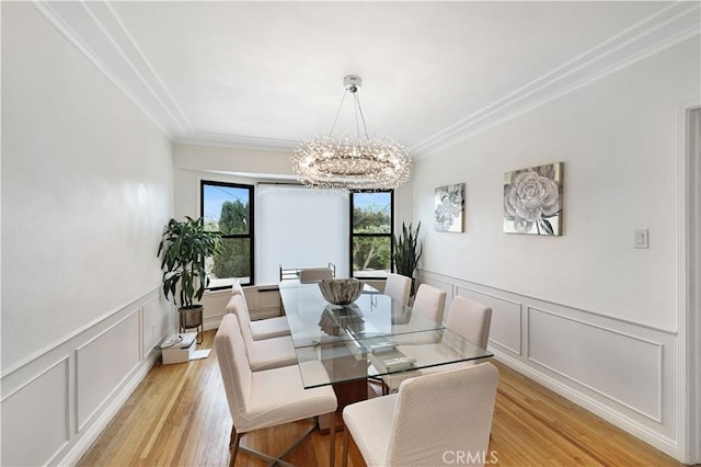 dining room featuring crown molding, light wood-style floors, a notable chandelier, and a decorative wall