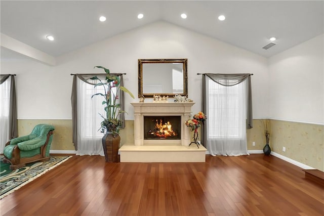 unfurnished room with a warm lit fireplace, visible vents, wood finished floors, and lofted ceiling