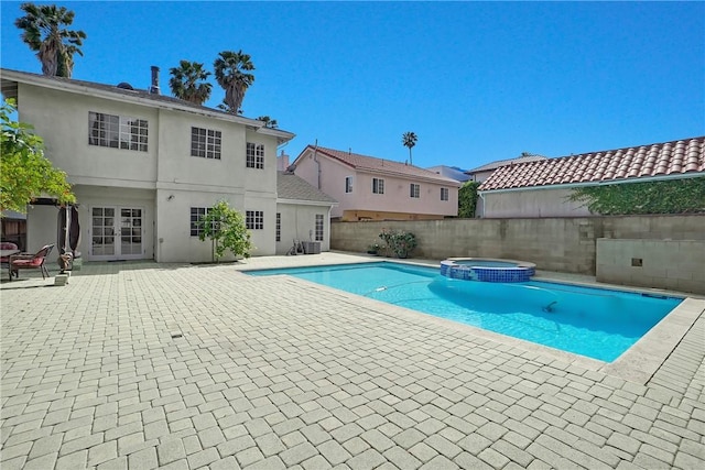 view of swimming pool featuring a fenced backyard, a patio area, a pool with connected hot tub, and french doors