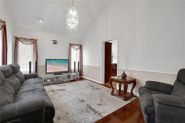 living area with high vaulted ceiling, a notable chandelier, a wealth of natural light, and wood finished floors