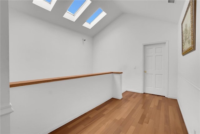 corridor featuring vaulted ceiling with skylight, baseboards, and wood finished floors