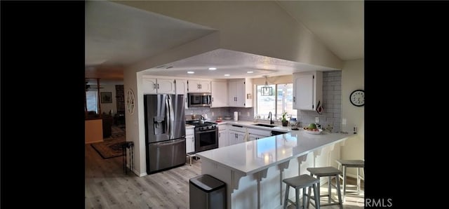 kitchen featuring decorative backsplash, a breakfast bar area, a sink, a peninsula, and stainless steel appliances