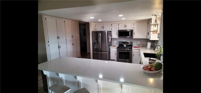 kitchen featuring a textured ceiling, appliances with stainless steel finishes, a sink, light countertops, and a peninsula