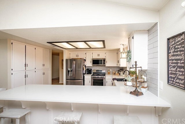 kitchen featuring tasteful backsplash, light countertops, a sink, a peninsula, and stainless steel appliances