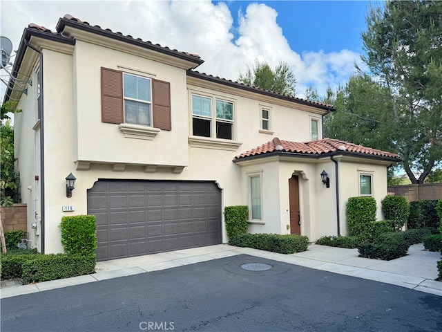 mediterranean / spanish-style home featuring an attached garage, stucco siding, a tile roof, and asphalt driveway