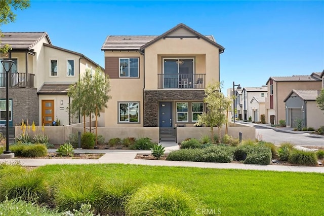 view of front of property with stucco siding, a front lawn, stone siding, and a balcony