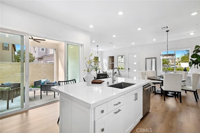 kitchen with a sink, dishwasher, light wood-style floors, white cabinetry, and visible vents