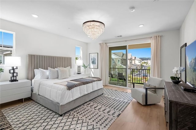 bedroom featuring access to outside, wood finished floors, multiple windows, and an inviting chandelier