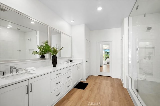 bathroom featuring double vanity, a shower stall, wood finished floors, a sink, and recessed lighting