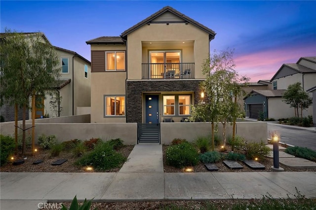 view of front of home with a balcony, stone siding, stucco siding, a gate, and a fenced front yard