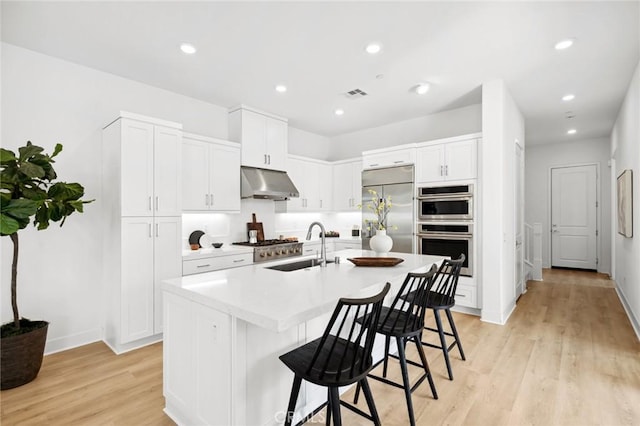kitchen with visible vents, light wood finished floors, under cabinet range hood, a breakfast bar, and stainless steel appliances