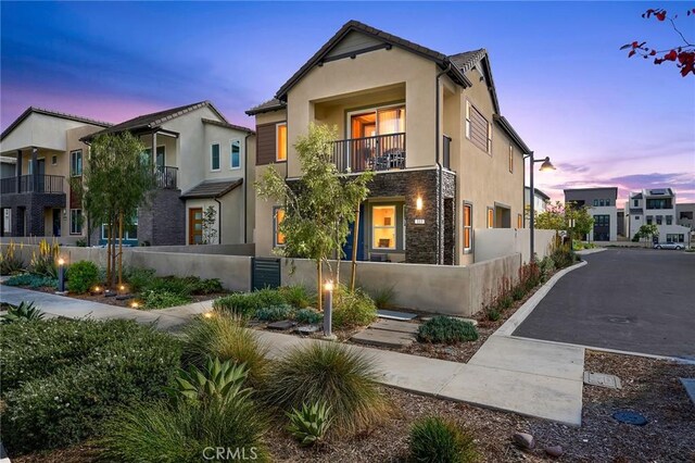 view of front facade featuring a fenced front yard, stucco siding, a balcony, and stone siding