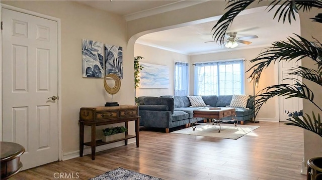 living area with crown molding, arched walkways, a ceiling fan, baseboards, and wood finished floors
