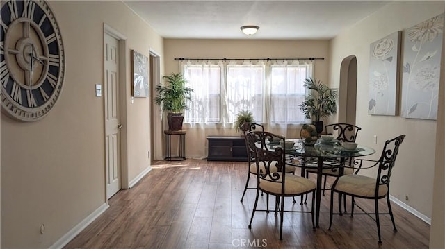 dining space featuring arched walkways, baseboards, and wood finished floors
