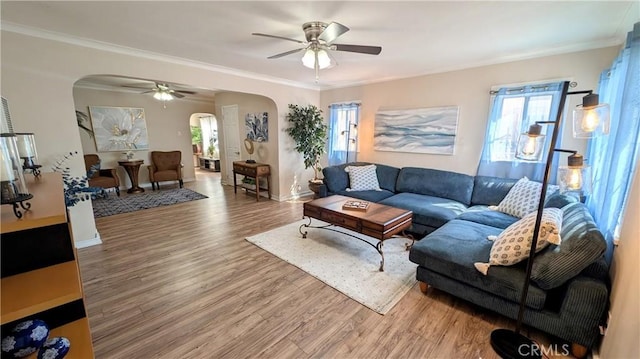 living room with crown molding, wood finished floors, baseboards, ceiling fan, and arched walkways