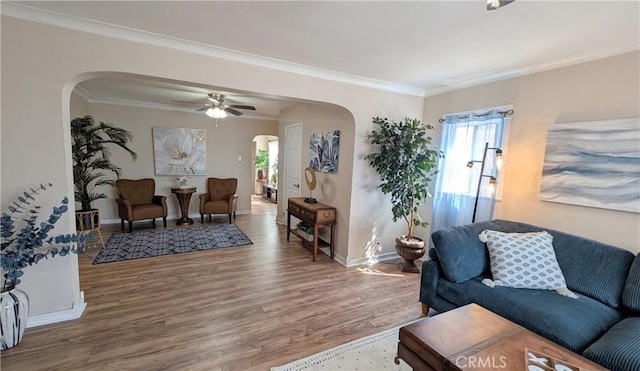 living area with crown molding, wood finished floors, baseboards, ceiling fan, and arched walkways