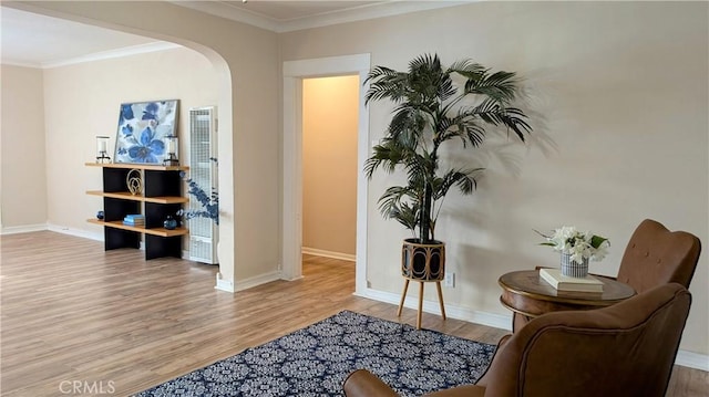 living area featuring crown molding, arched walkways, baseboards, and wood finished floors